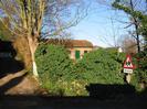 Driveway with white gates, ivy hedge, barn on village green, and road sign
warning of school.