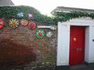 Main entrance to The Old Rectory. Red door in white surround, with etched copper
plate. High wall with hubcaps found and decorated by Sheila Horton,
and sign saying `Vaccinate not Exterminate'
(protest at official handling of Foot and Mouth outbreak in 2001)
