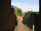 Passage between houses.
Brick walls on the left, and fence on the right.
Trees and street light.