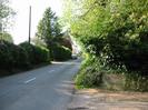 Road with hedges and telephone pole on the left.
Low brick wall on right with Hitcham Grange sign.
Bushes overhanging the wall.