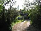Gravel drive between bushes leading to bungalow.
Church Spire visible above roofline.