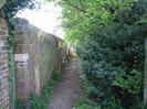 Footpath with high brick wall on the left and bushes on the right.