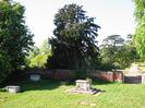 The north-west corner of the old churchyard.
Grassy area with grave markers.
High brick wall with garden and trees beyond.