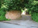 The entrance to Elibank Court.
High brick wall on the left with ivy and overhanging trees.
Tarmac driveway rises as it curves to the left.
Wooden gates.