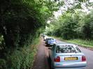 Looking north on Station Road.
Trees on both sides.
Tarmac footpath and parked cars on the left.