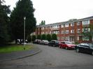 Hillmead Court: three storey flats.
Built of red brick, with white window frames and doors.
Low-pitched grey roof.
Trees and street-light in front of flats.
Parked cars.