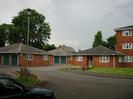 Blocks of garages onthe left with trees behind.
Hillmead Court flats on the right.
Street-light in verge.