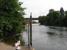 River Thames with railway bridge in the background.
Man and boy fishing.
Wooden mooring posts in river.
Trees and boats.