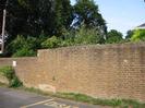 High brick wall with trees behind.
Disabled parking space marked on road in foreground.
Telephone pole on left.