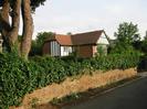 Wall along road with ivy growing over it.
New mock-tudor house behind wall.