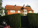Harefield.
Two-storey house hung with red tiles.
Red tile roof.
High clipped hedge with green wooden gate.
Parked motorcycle.