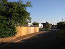 Looking south on Hitcham Road.
Wall and fence on left with bushes behind.
White houses in the distance on the left.
Grass verge on the right.