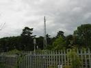 Metal paling fence with railway and cellphone mast beyond.
Trees in the background.