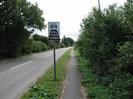 Looking south on Marsh Lane.
Trees on left of road.
Grass verge with footpath and trees on right.
Sign in verge 'KILL YOUR SPEED'.