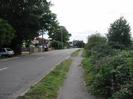Looking south on Marsh Lane.
Fences and driveways on left of road, with some large trees.
Houses visible in the distance.
Roadsign warning of double bend.
Grass verge with footpath and bushes on right.