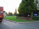 Junction with A4 Bath Road and entrance to the Bishop Centre.
Lorry on left.
Wide grass verge.
Wall and fence with trees behind.