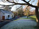 Rectory Road passing the Village Green.
White and cream-painted houses.
Trees on the green and beyond.
Frost on grass, road, and roofs.