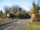 Approaching the village on Boundary Road.
Speed-limit signs on poles.
SLOW and 30 road markings.
Wall and trees in the background.