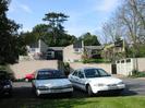 Car park and garages at Eastern end of Cedar Chase.
Parked cars in foreground, rear of houses 20, 19, and 18 behind.
Large Cedar trees in the background are on the other side of Rectory Road.