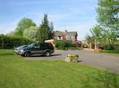 Road leading to St Nicolas School and Village Hall.
Stone tub of flowers.
Parked cars.
School House in the background.