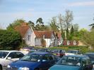 The Village Hall car park.
Houses with tile roofs in the background.
Hill House just visible through the trees.
