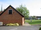 Western end of the Village Hall.
Sacks of building materials.
Part of the Village Green with people.
St Nicolas Church spire visible on the left.
Oak and Saw public house and houses on Rectory Road visible beyond the Village Green.