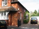 Rozel. Red brick house with tile roofs including some patterned tiles.
Driveway to garages.
Parked cars.
Trees visible above garages.