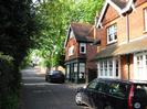 Looking North on High Street.
Dark hedge on the left.
Red brick houses on the right.
House in centre of picture is tile-hung at first-floor level, and has shop-front windows (this used to be the village Post Office).
Trees overhanging the road.
Parked cars.