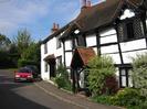 White house with black door.
Cottage with white walls and black timbers.
Shrubs, parked cars.