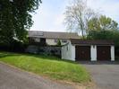 Driveways and white garages with black doors.
House visible over wall has grey roof with solar collectors.
Large trees.