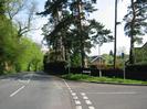 Road junction with street sign for High Street.
Wall and trees on left.
Large Scots Pine trees on right.
30-limit repeater sign and `Unsuitable for heavy vehicles' sign.
SLOW marking on Hill Farm Road.
Street light with water-company markers on the pole.