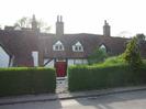 Cottages with white walls, black timbers, and tile roofs.
Hedge with white gate leading to red front door.