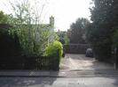 Wooden fence with trees behind, and house visible through them.
Gravel drive.
Larger trees on the right.