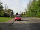 Looking North on Hill Farm Road.
Grass area on left with streetlight.
Parked Cars.
Traffic-calming road markings.
Houses visible in the distance.