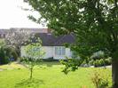 Cream-painted bungalow with tile roof.
Grass area with trees.
Child playing.
Rear of houses in Buffins visible on left.