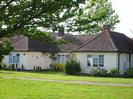 Cream painted bungalow with tile roof.
Grass area with trees in front.