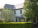 Harbinger: cream-painted house with sash windows and slate roof.
Trees and hedge in front.
Wrought-iron gate in hedge.