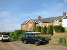 Houses built from sandy brick with slate roofs.
Hedges and shrubs in fornt of houses.
Parked cars.
Telephone junction cabinet.