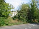 Looking across Hill Farm Road from the corner of High Street.
Bank with trees.
Part of Hitcham Grange visible through the trees.
SLOW marking on road.
High brick wall on the right.
