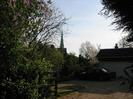 Entrance to Allington Cottage.
Bushes on the left, with wooden gate.
St Nicolas Church visible on the skyline.
Car and garage on the right, with gravel drive.