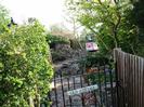 Path to Old Cottage.
Iron gate with nameplate.
Hedge on the left with lamp-post just visible beyond.
Path with pile of earth and mini-digger.
Wooden fence and small trees on the right.