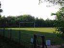Playing field with low chainlink fence and football goalpost.
Trees beyond.