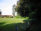 Playing field with football goal.
Roof of long low house on the left.
Large trees.
Low chainlink fence.