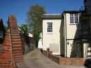 High brick wall on left, Cream-coloured house on right.