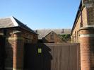 Wooden gate set between round brick pillars.
Buildings and slate roofs beyond.