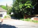 View across Berry Hill.
Part of white bungalow on left.
Entrance road with portico.
Large trees on right overhang red-brick wall with decorative pillars.