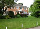 Grassy bank with low fence.
Large mock-Georgian house behind row of bushes.