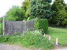 Wooden slat fence on left with large trees behind it.
Low post and chain fence on the right with grassy bank and trees.