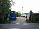 Boatyard entrance.
Gates set between high brick walls.
Large blue skip.
Boats and crane.