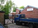 Low brick buildings with iron gates and blue pick-up truck.
Sign on wall: "MAIDENHEAD SEA CADETS / T.S. IRON DUKE"
Trees in background.